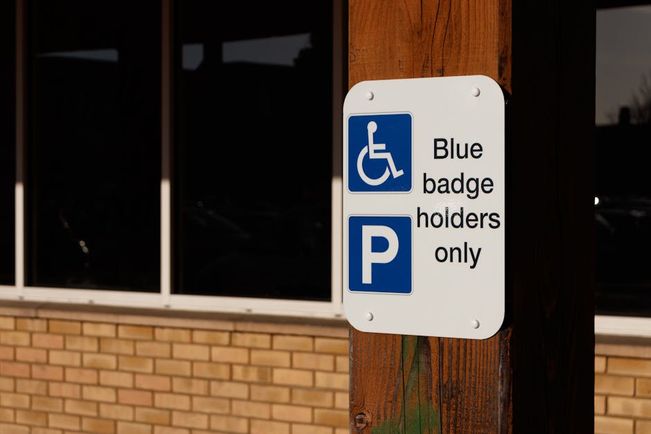 A close-up view of a neon green illuminated sign reading 'Parking' with an arrow pointing to the left, mounted on a grey metal frame attached to the exterior of a modern multi-story building made of l