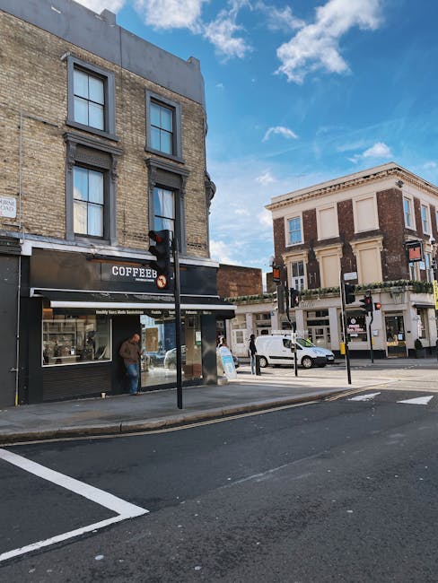 A street view on West Green Road featuring a two-storey brick building on the left with a black and white storefront labeled 'COFFEE B' and a large window display, with a person standing just outside 
